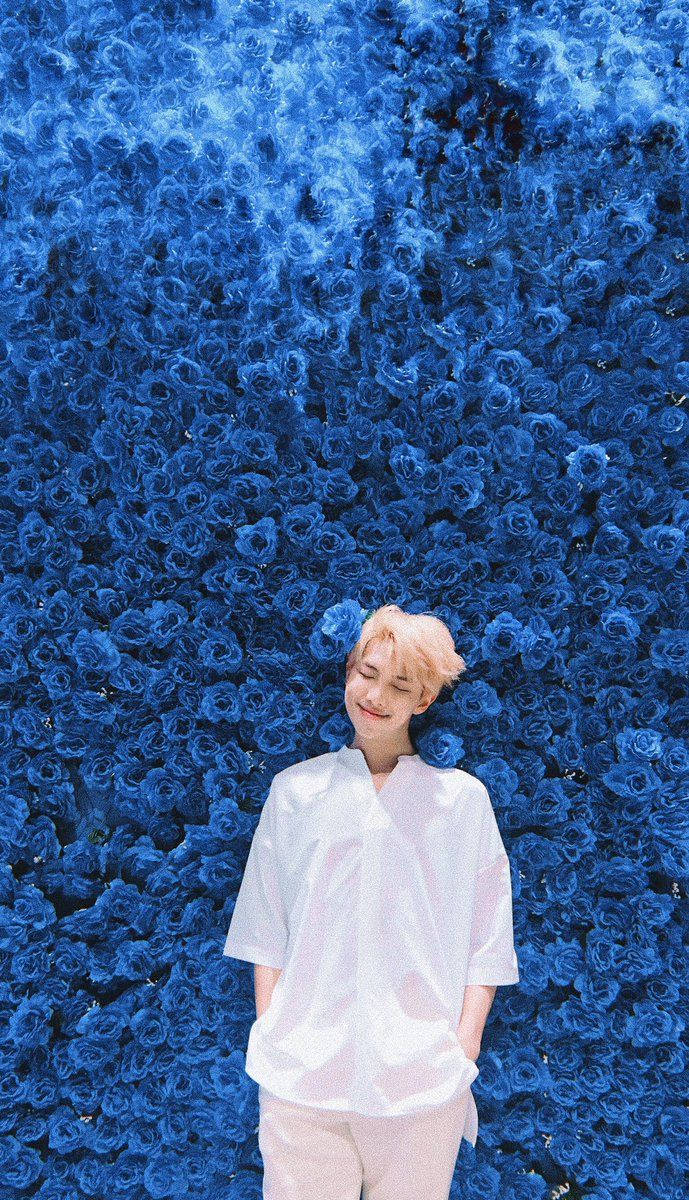 BTS सदस्य नीले फूलों से भरी दीवार के सामने खड़ा है। — बीटीएस वॉलपेपर
