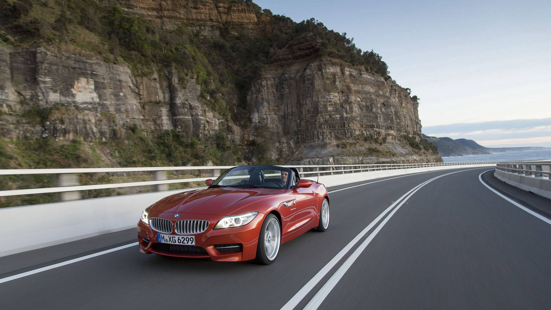 पहाड़ के बगल में सड़क पर ऑरेंज BMW Z4 कार का वॉलपेपर — Bmw वॉलपेपर