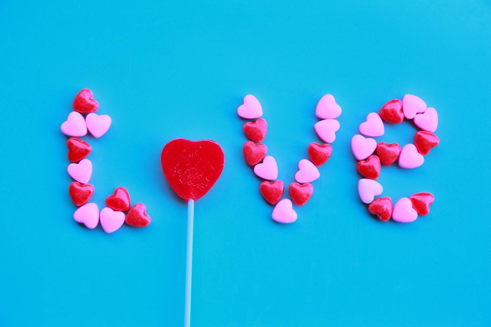 वैलेंटाइन डे के लिए चमकीली नीली दीवार पर शब्द love बनाते गुलाबी और लाल कैंडी हार्ट रॉक्स। — प्यार वॉलपेपर