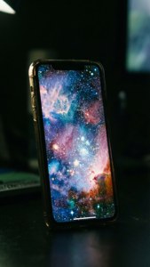 iPhone 17 की स्क्रीन अंधेरे में गैलेक्सी वॉलपेपर के साथ चमक रही है।