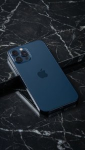 मार्बल पर मिडनाइट ब्लू रंग का iPhone 17, मिनिमलिस्ट स्टूडियो शॉट।